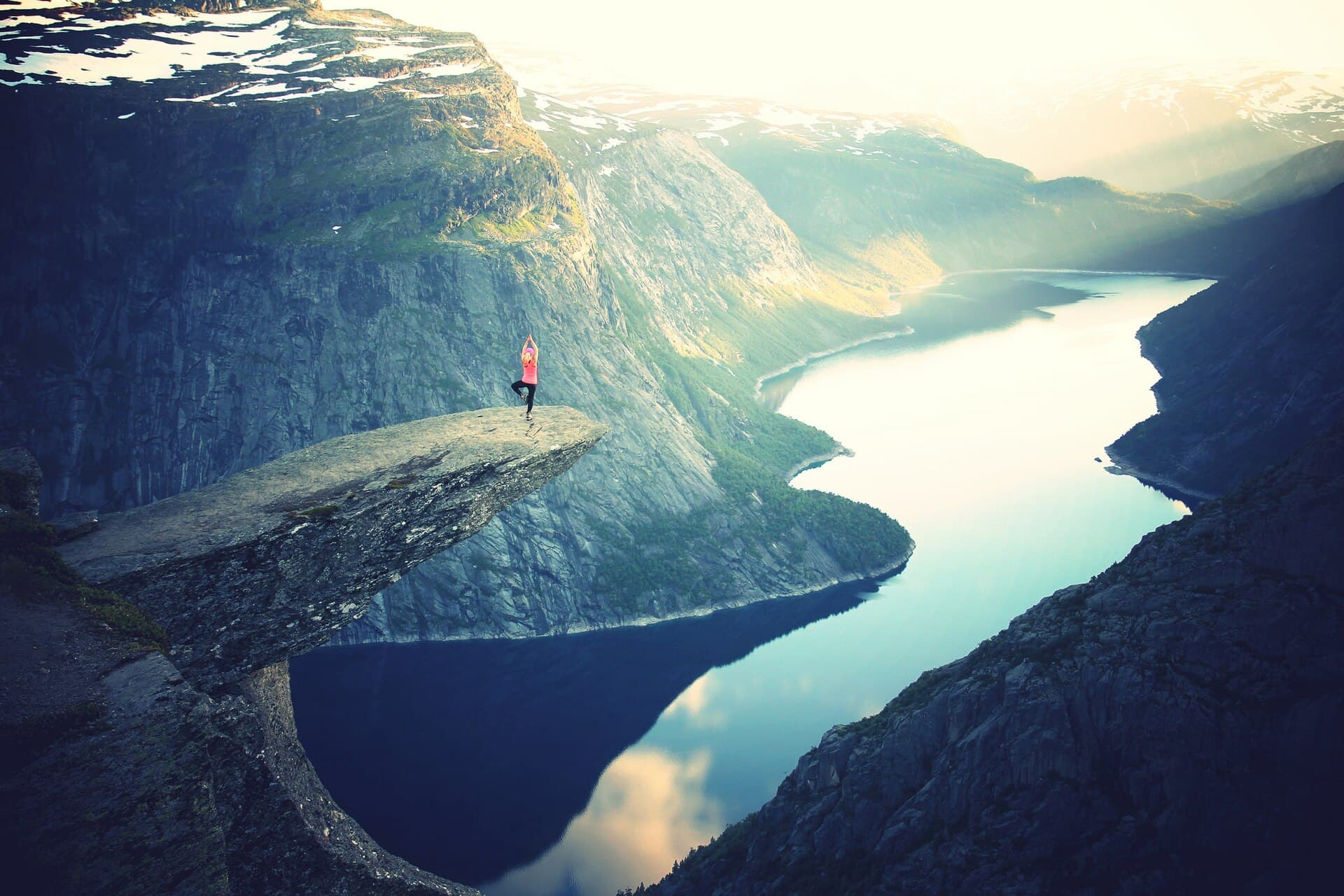 A hiker on Trolltunga above the sunlit lake and steep mountains of Norway